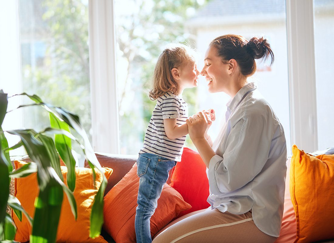 Read Our Reviews - Portrait of a Cheerful Mother Playing with her Young Daughter as they Spend Time Together in the Living Room on the Sofa