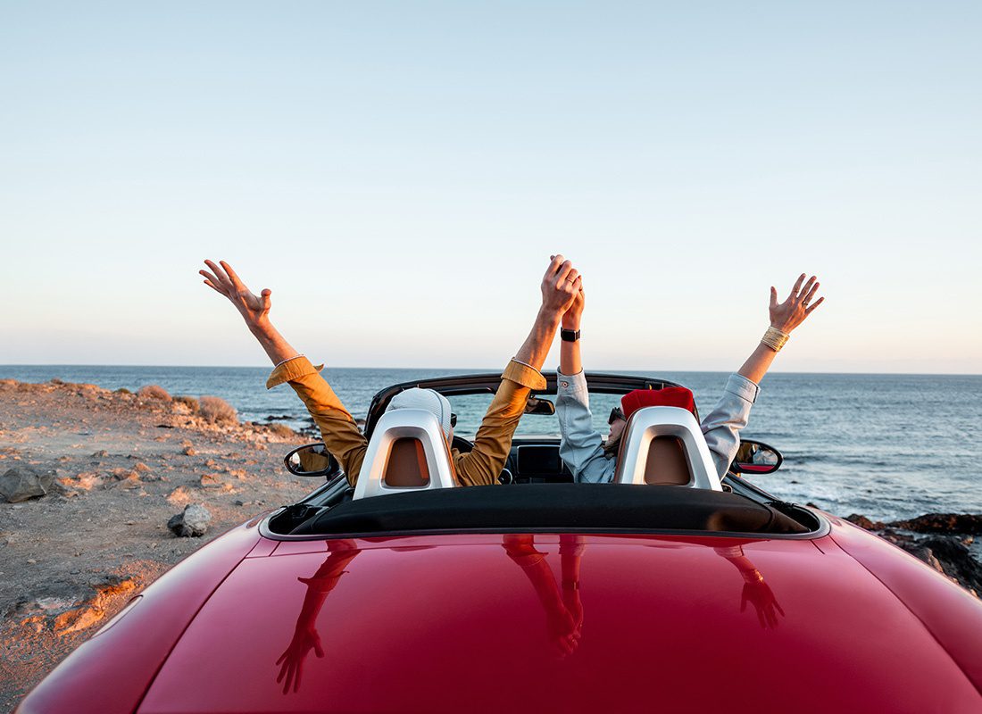 Service Center - Rear View of a Cheerful Couple With Their Hands Up in the Air Sitting in a Red Convertible on a Road Trip to the Coast